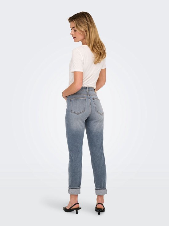Vrouw in een spijkerbroek met omgeslagen pijpen en zwarte slingbacks, haar handen in haar zakken.