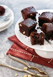 Stukjes donkere chocoladebrownie met hazelnoten op een witte taartstandaard met een metalen vork.