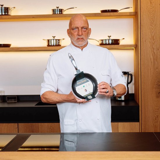 Chef in wit koksuniform houdt zilverkleurige koekenpan met productinformatie omhoog.