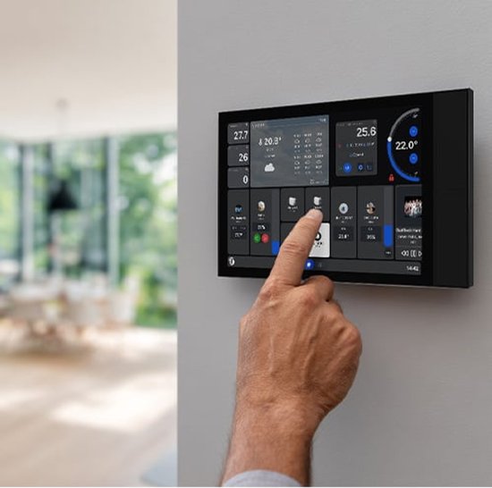 Een hand raakt het scherm aan van een zwart Shelly Wall Display XL, gemonteerd op een muur in een moderne woonkamer.