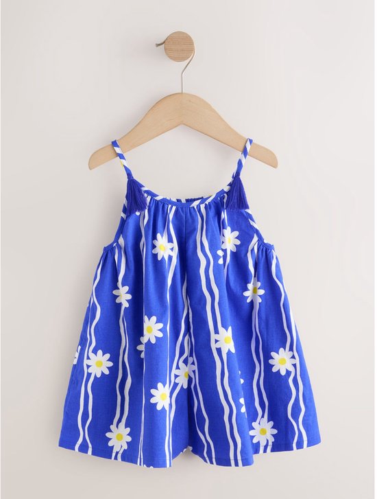 Blauw playsuit met spaghettibandjes, witte bloemen en golvende strepen, hangend aan een houten kledinghanger.