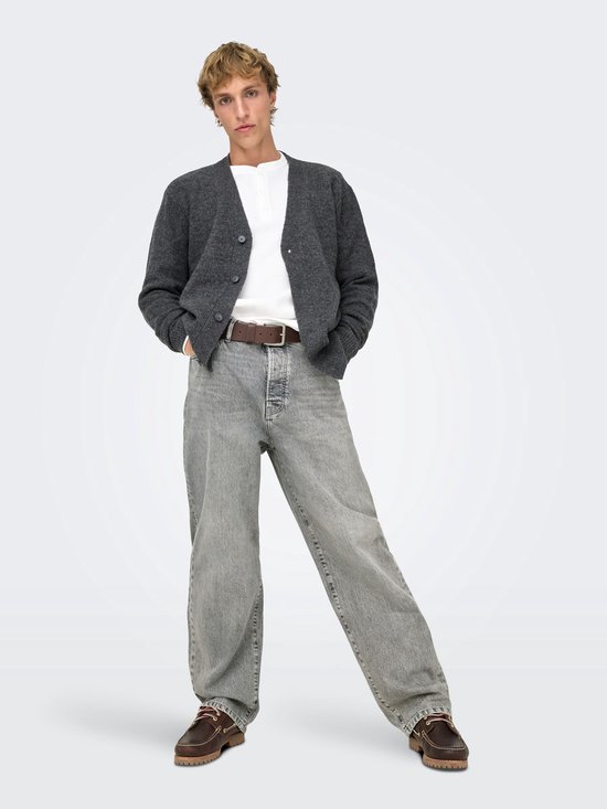 Een man draagt een grijze jeans met rechte pijpen, een wit shirt, een grijze vest en bruine instappers.