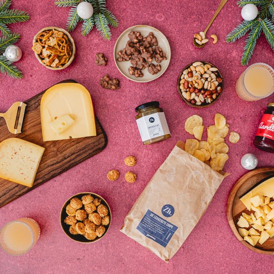 Kerst borrelplank met kazen, worstjes, crackers, chips, noten, dips en sapjes op een roze tafelkleed.
