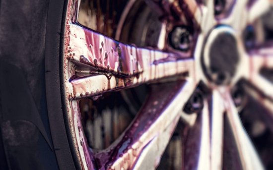 Dichtbij van een vieze auto velg met paarse reiniger, detail van de spaken en remklauw.