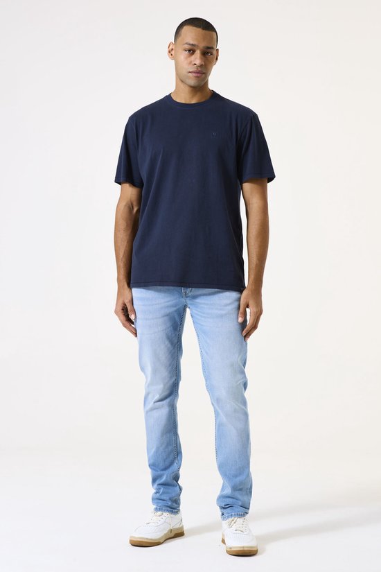 Man met donkere huid in een donkerblauw T-shirt en lichtblauwe spijkerbroek.