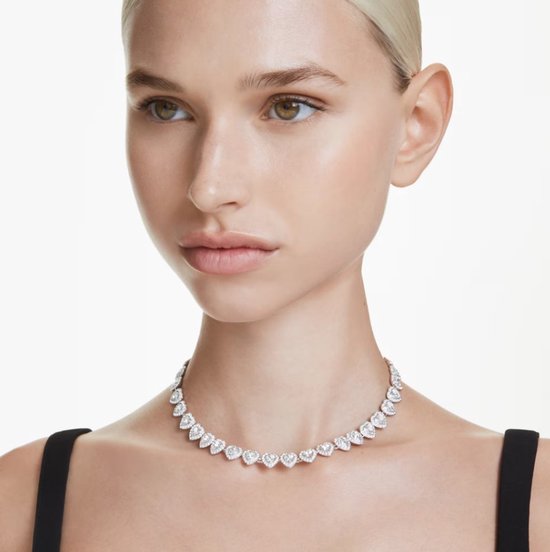 Model draagt een zilverkleurige ketting met hartvormige kristallen.
