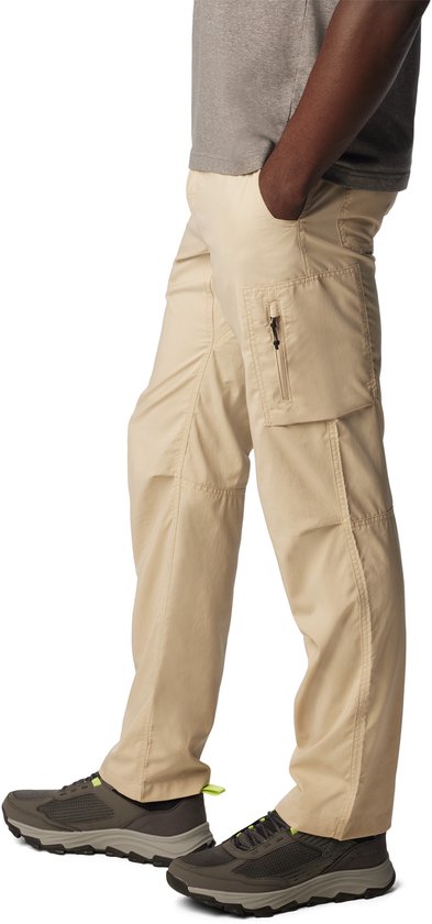 Man met een beige cargobroek, met een ritszakje op de dij, de broek is gedragen met grijze sneakers met groene accenten.