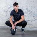Man in zwarte sportkleding poseert gehurkt naast een zwarte kettlebell.