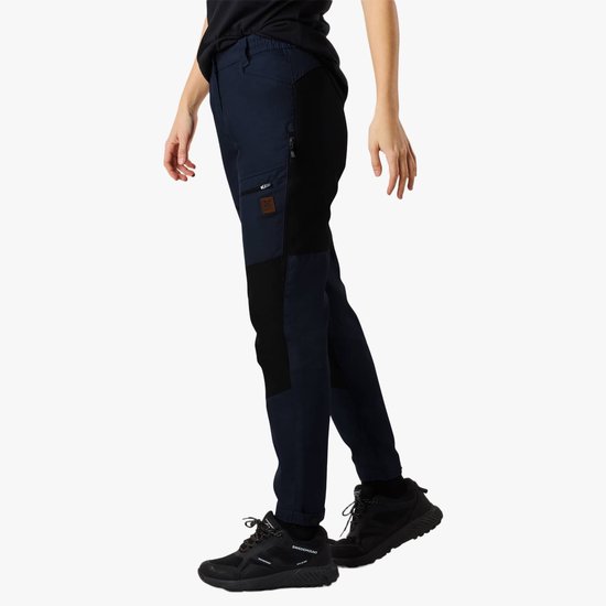 Vrouw draagt een donkerblauwe outdoorbroek met zwarte panelen, met ritssluitingen op de zakken en drukknopen aan de onderkant.