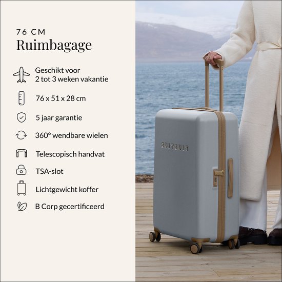 Grote lichtgrijze koffer met gouden details, gedragen door een vrouw met een witte jas.