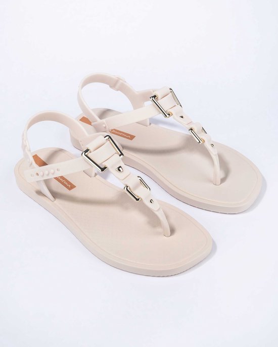 Paar lichtbeige Ipanema slippers met gouden gespen en bandjes over de wreef en rond de enkel.