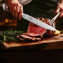 Un chef coupe une viande rôtie avec un couteau de cuisine japonais damassé à manche en bois.
