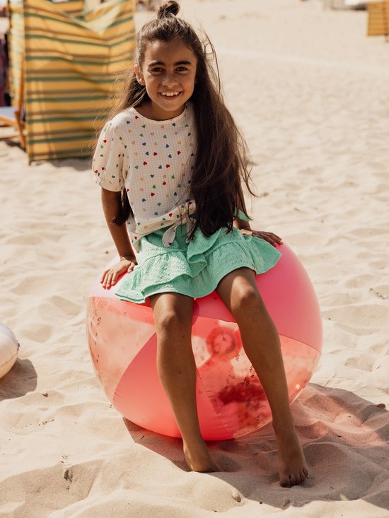 Meisje met lange bruine haren zittend op een roze strandbal met een top met hartjesprint en mintgroene rok met ruches.