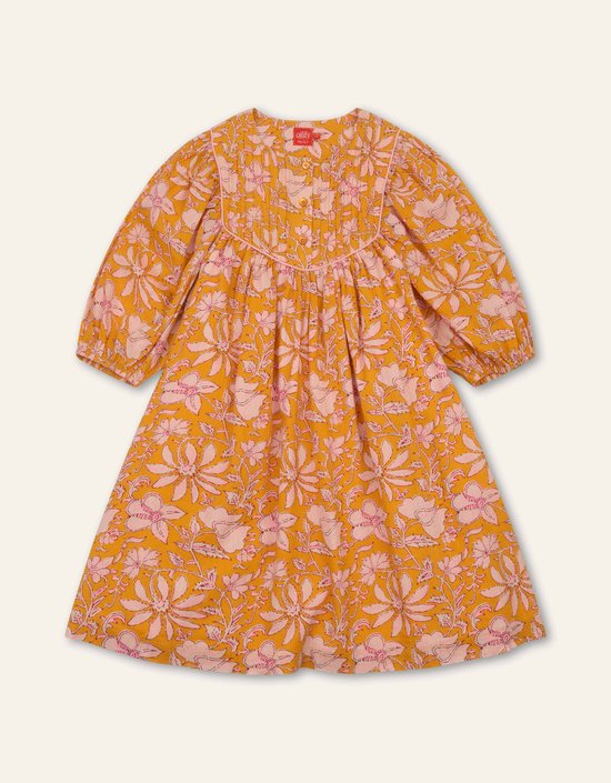 Voorkant van de okergele jurk met roze bloemen, geplooide borstpartij, roze biesjes en Oilily label.