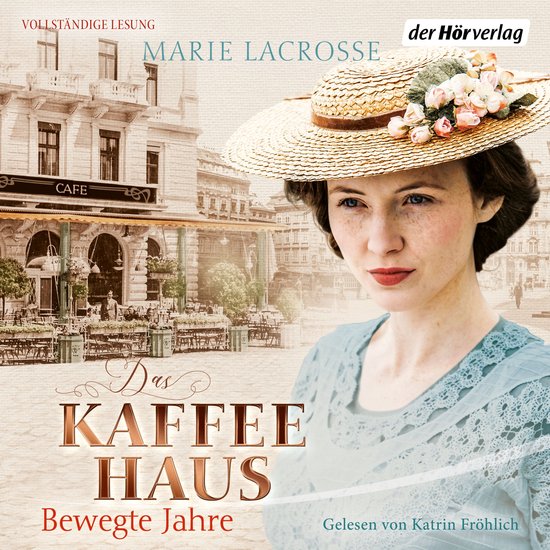 Une femme rousse porte un chapeau de paille orné de fleurs et une robe bleue en dentelle. Un café en arrière-plan.