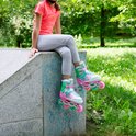Meisje met roze skeelers met zeemeerminnen-thema, zittend op een betonnen rand in een park.