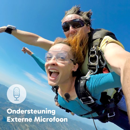 Parachutisten springen uit een vliegtuig, de vrouw draagt een blauw shirt en een externe microfoon.