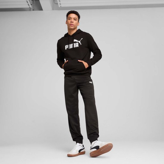 Man in een zwarte PUMA hoodie met wit logo en zwarte joggingbroek, staand.