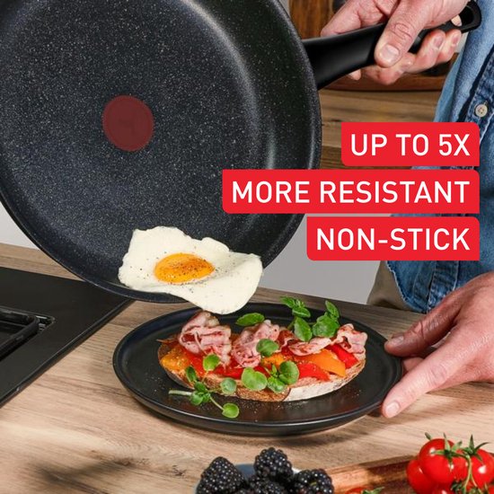 Hand die een zwarte koekenpan met anti-aanbaklaag omkeert boven een bord met toast, ei en zalm.