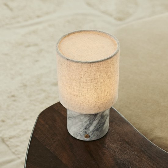 Marmeren tafellamp met beige linnen kap staat op een donkerhouten bijzettafel.