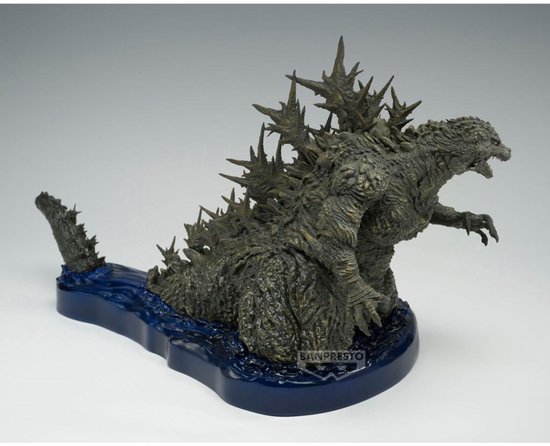 Grijze Godzilla figuur met scherpe rugplaten, op een blauwe waterbasis met logo.