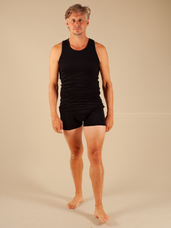 Man met grijs haar in een zwarte tanktop en zwarte boxershorts.