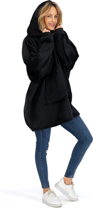 Een vrouw in een zwarte, oversized fleece hoodie, met een capuchon en jeans.