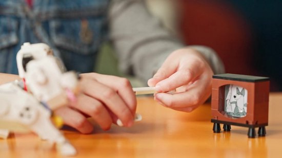 Handen bouwen aan een LEGO Dalmatiër bij een televisie.