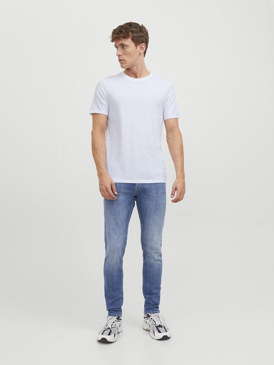 Man kijkt weg, draagt een witte T-shirt, blauwe jeans en sneakers.