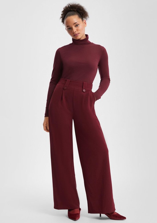 Model draagt een bordeauxrode coltrui en een bordeauxrode wijde broek met hoge taille.