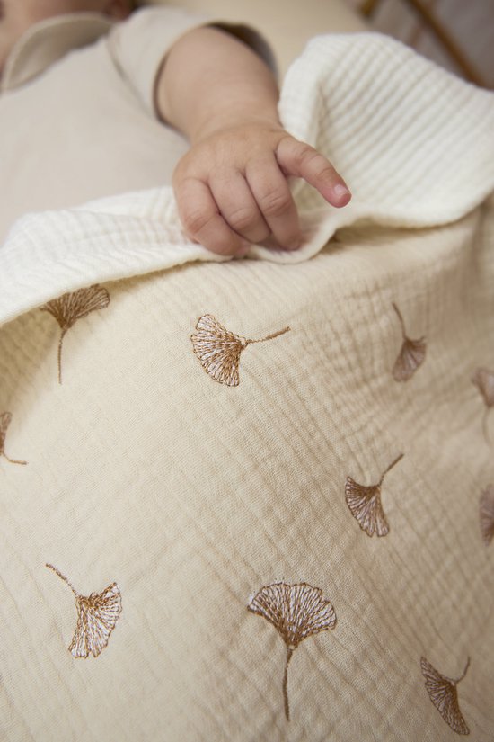 Witte hydrofiele deken met bruine ginkgo bladeren print, babyhandje op de deken.