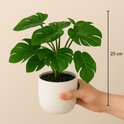 Een hand houdt een witte gespikkelde pot met een Monstera kunstplant van 25cm hoog.