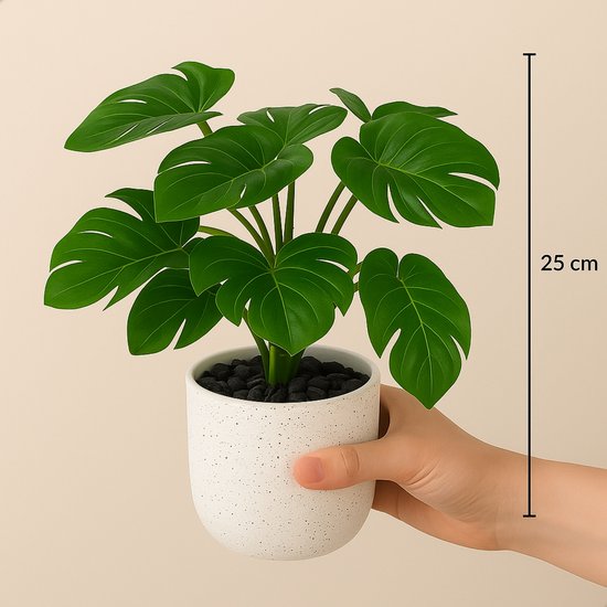 Een hand houdt een witte gespikkelde pot met een Monstera kunstplant van 25cm hoog.