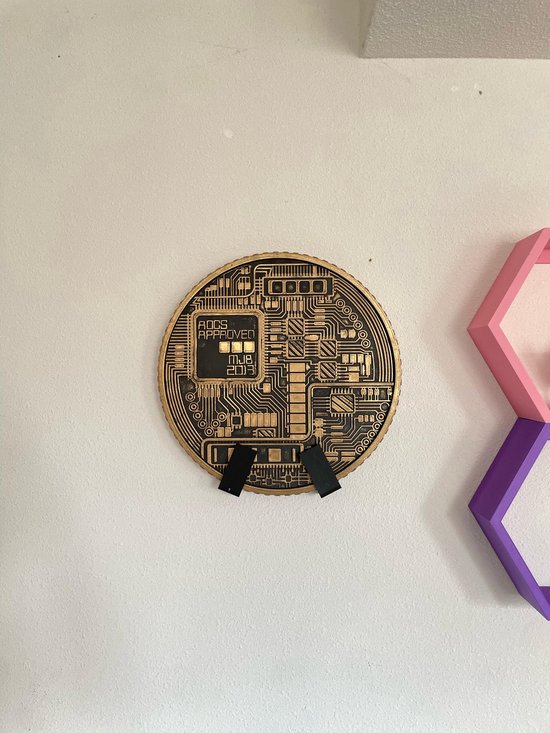 Goudkleurige Bitcoin-munt met "FODS APPROVED MJB 2018" en een circuitbord-ontwerp, bevestigd aan een muur.