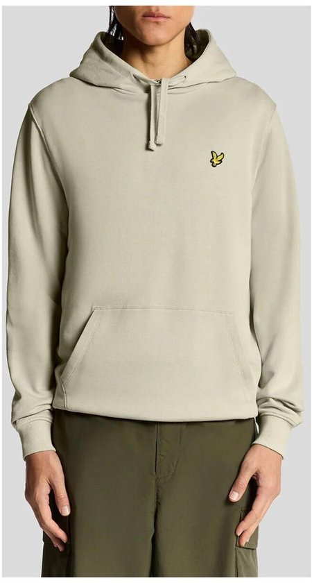 Model in beige hoodie met geel vogellogo, met donkergroene cargo broek.