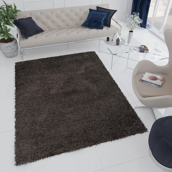 Tapis shaggy gris foncé dans un salon lumineux, près d'un fauteuil et d'une table d'appoint.