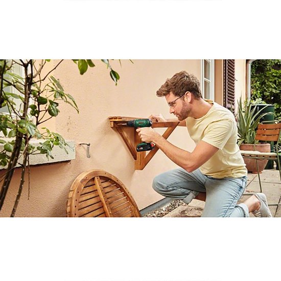 Man met bril en Bosch EasyDrill 18V-40 accuboormachine monteert een houten wandrek.
