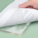 Een hand die wit papier optilt, waardoor tekst en een glanzende afdruk van tekst op een transparante plaat zichtbaar worden.