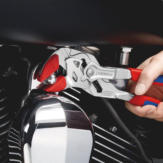 Hand houdt een tang met rode en blauwe handvatten vast, die een deel van een motorfiets aanpast.