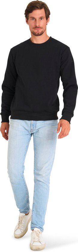 Man van voren, draagt een zwarte sweater en lichtblauwe jeans.