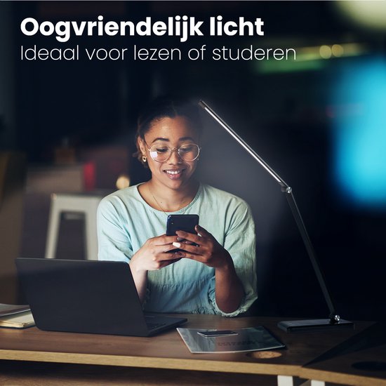 Vrouw met bril gebruikt smartphone naast zwarte Auronic bureaulamp, laptop erbij. Oogvriendelijk licht.