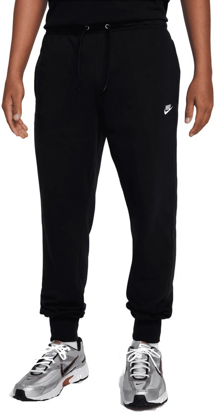 Man in zwarte Nike joggingbroek met trekkoord en klein Nike logo, gedragen met zilverkleurige sneakers.