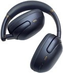 Gevouwen donkerblauwe JBL Tour One M3 koptelefoon met gouden details, op witte achtergrond.