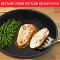 Zwarte pan met kippenborst, sperziebonen en erwten, bestand tegen metalen keukengerei.