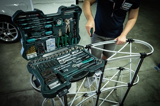Een man gebruikt een schroevendraaier uit een open, donkergroene gereedschapskoffer om een metalen frame in elkaar te zetten.