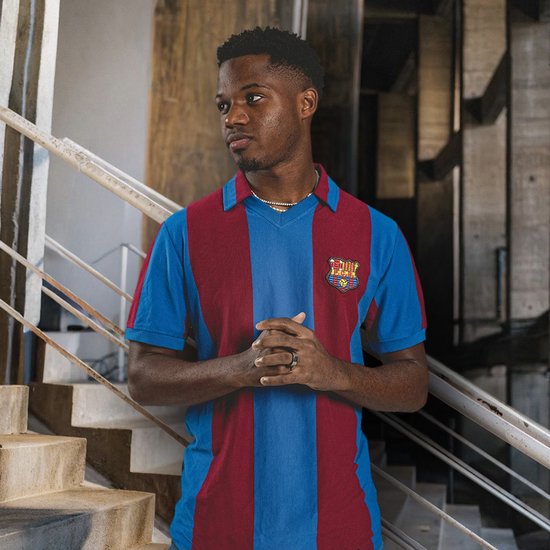 Jonge man met een donkere huid en een FC Barcelona shirt met verticale blauwe en bordeauxrode banen, staand op een trap