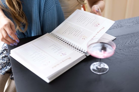 Twee vrouwen bladeren door een open ringband-planner met lijsten en vakken.