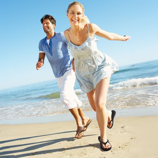 Vrolijk lachend stel op het strand, de vrouw draagt een zomerse jurk, de man een blauw shirt.