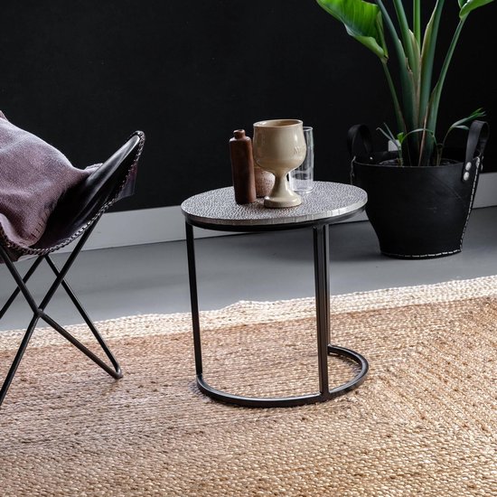 Ronde bijzettafel met gevlekt blad en zwart metalen frame, naast vlinderstoel.