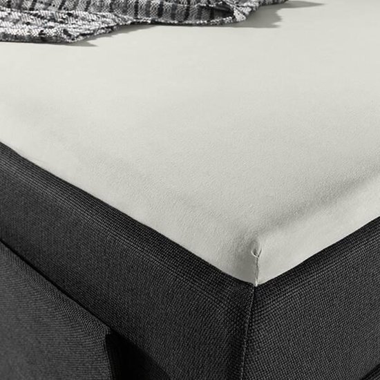 Detail van de hoek van een donkergrijs bed met een crème splittopper hoeslaken.